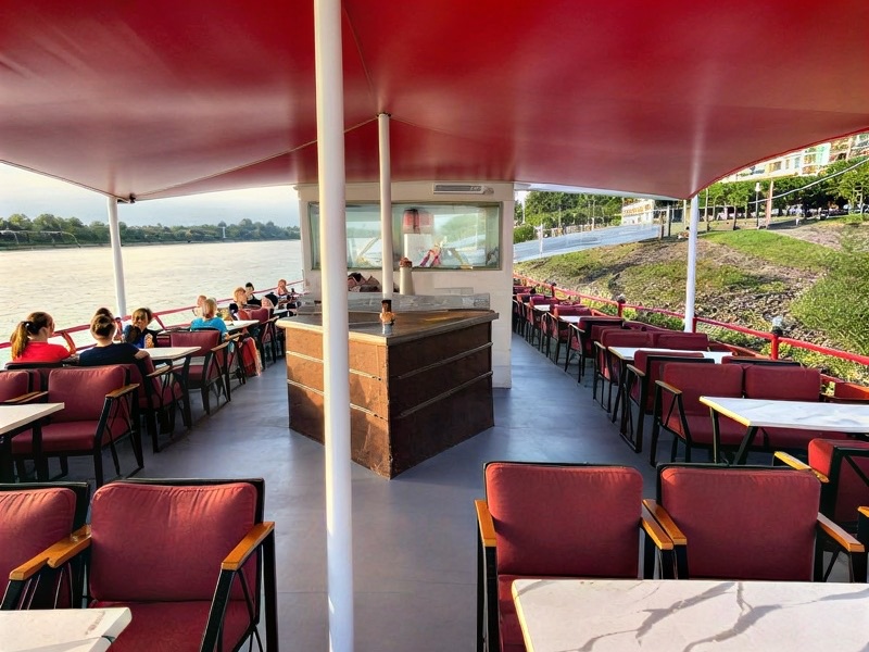 Gedeckte Tische an Deck unter roten Sonnenschirmen mit Blick auf den Rhein